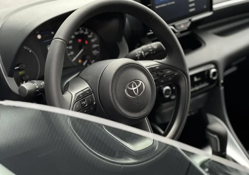 Vue rapprochée du volant en cuir noir d'une Toyota Yaris hybride 2025, avec commandes multifonctions visibles.