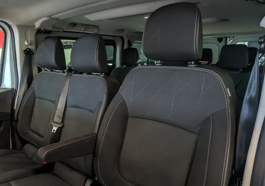 Vue intérieure rapprochée des sièges avant en tissu noir du Renault Trafic Combi 2025, avec accoudoir côté droit.