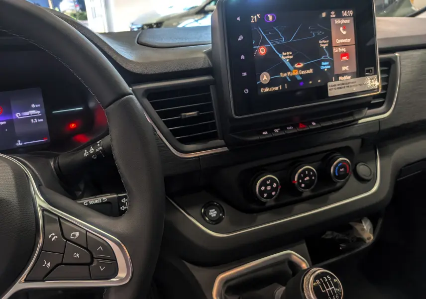 Vue rapprochée de l'intérieur du Renault Trafic Combi 2025, tableau de bord noir avec écran tactile et levier de vitesses manuel.