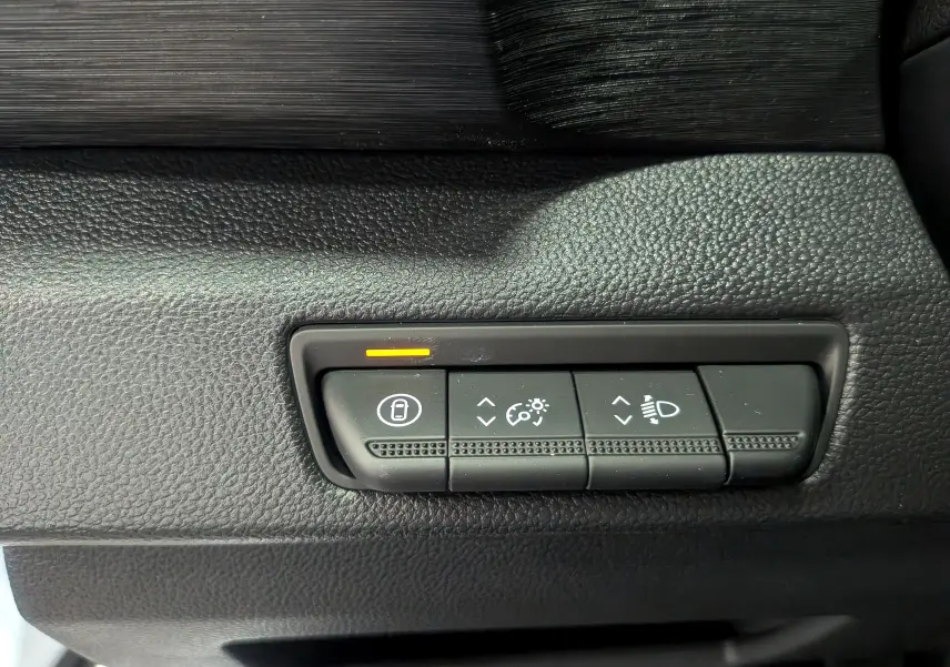 Gros plan sur les commandes de réglage des phares et verrouillage dans l'habitacle noir du Renault Trafic Combi blanc.