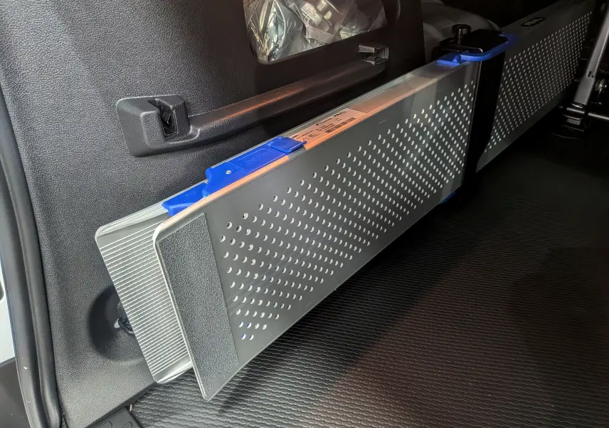 Détail intérieur montrant une rampe pliante grise avec poignée bleue dans un Renault Trafic Combi blanc.