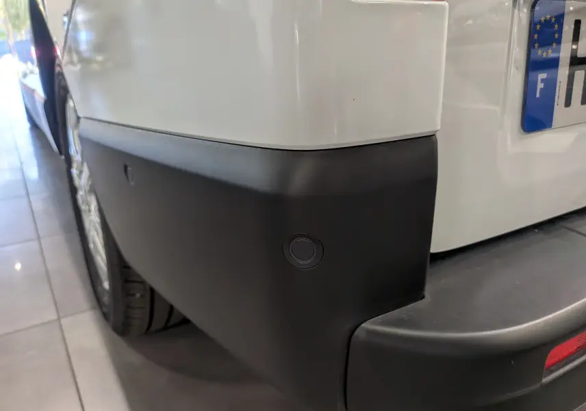 Gros plan sur le pare-chocs arrière droit blanc glacier du Renault Trafic Combi avec capteur de recul visible.