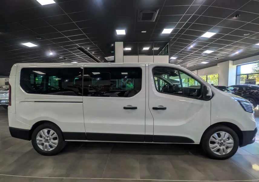 Profil latéral droit du Renault Trafic Combi blanc Glacier 2025 en showroom, avec vitres teintées et jantes alliage.