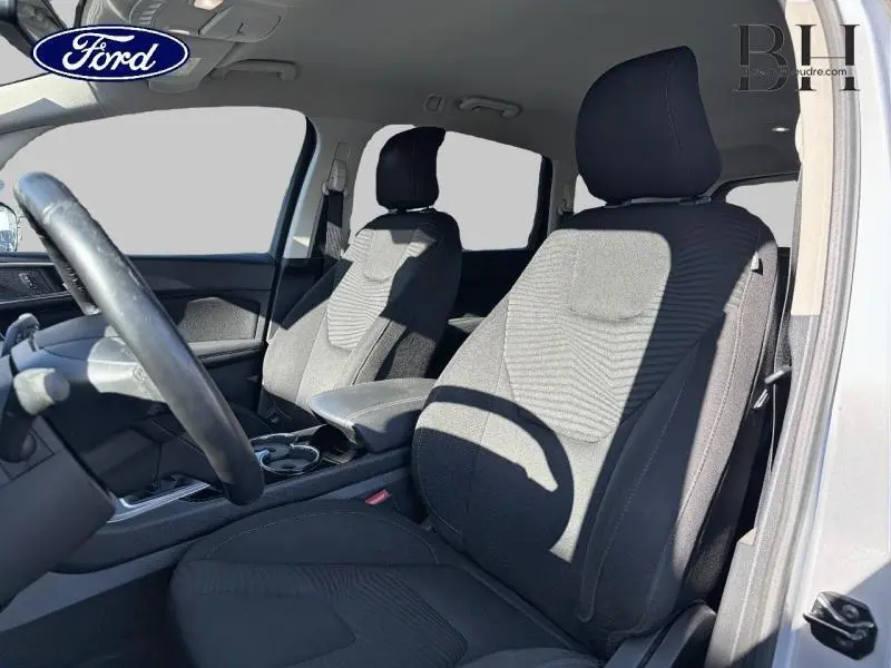 Vue intérieure côté conducteur du Ford S-MAX gris lunaire, montrant les sièges avant en tissu et le volant cuir.