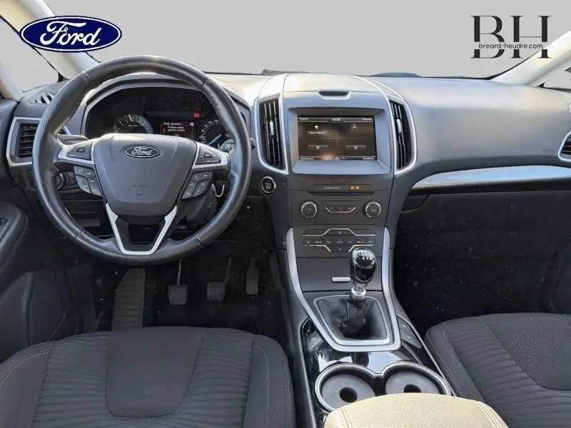 Vue intérieure avant du Ford S-MAX gris lunaire, montrant le volant cuir, tableau de bord et levier de vitesses manuel.