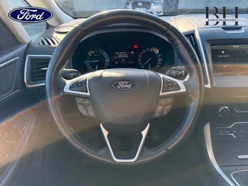 Vue rapprochée du volant cuir noir de la Ford S-MAX 2016 avec commandes intégrées et tableau de bord digital.