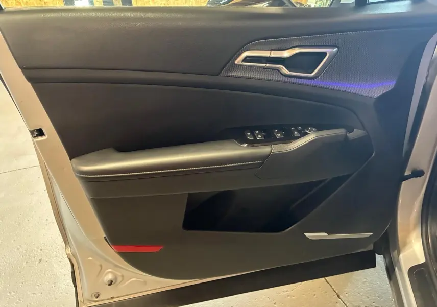 Vue intérieure sur la porte avant gauche du Kia Sportage gris 2024, avec commandes de vitres et poignée métallique.