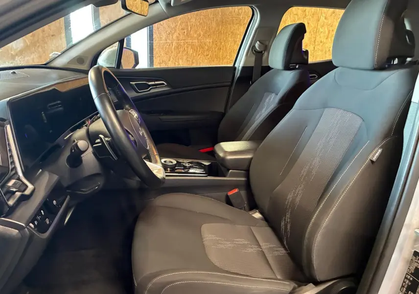 Vue intérieure côté conducteur du Kia Sportage 2024 gris, montrant sièges noirs et tableau de bord moderne avec écran tactile.