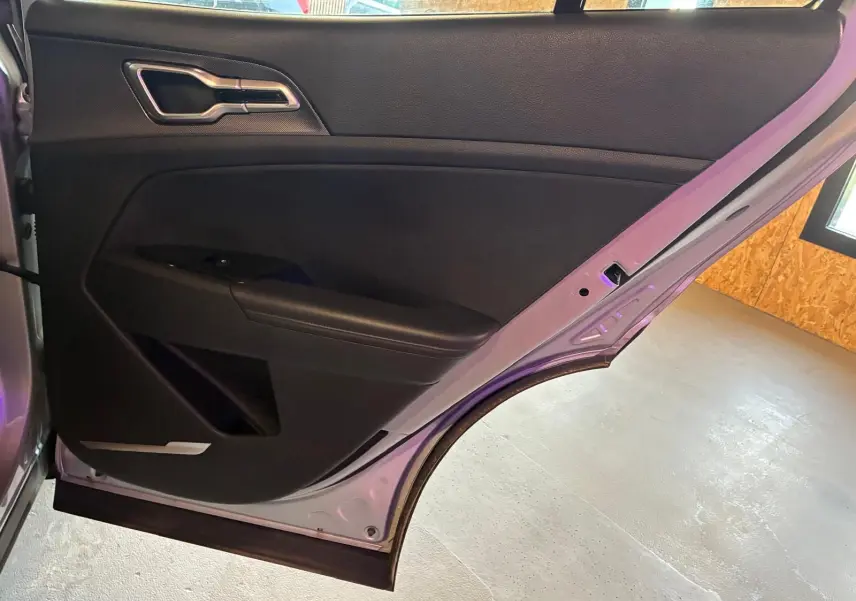 Vue intérieure de la porte arrière gauche du KIA Sportage gris 2024, avec poignée argentée et accoudoir noir.
