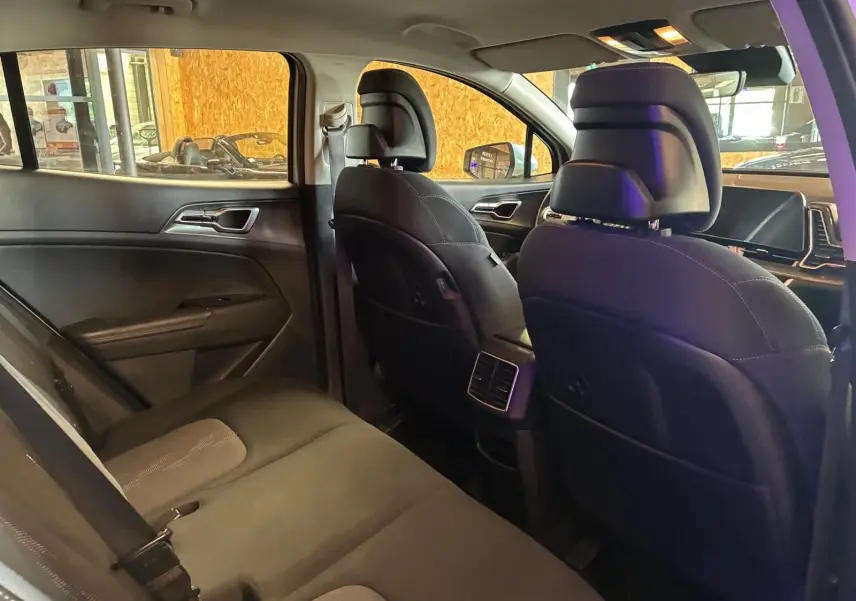 Vue intérieure arrière du Kia Sportage 2024 hybride, sièges noirs avec surpiqûres et aérateurs centraux visibles.
