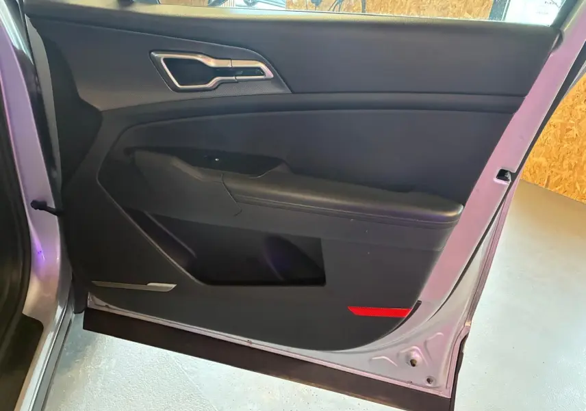 Vue intérieure de la porte avant gauche d’un KIA Sportage gris 2024, avec garniture noire et poignée argentée.