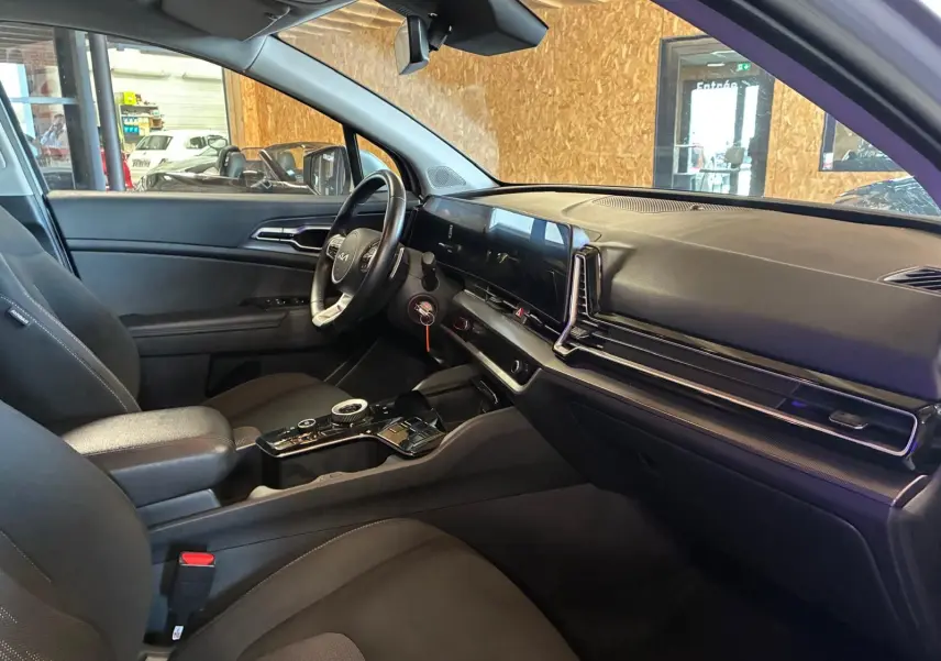Vue intérieure côté conducteur du Kia Sportage hybride 2024, avec tableau de bord moderne et sellerie noire.