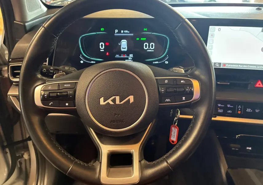 Vue rapprochée du volant noir du Kia Sportage 2024 hybride avec tableau de bord numérique et écran tactile.