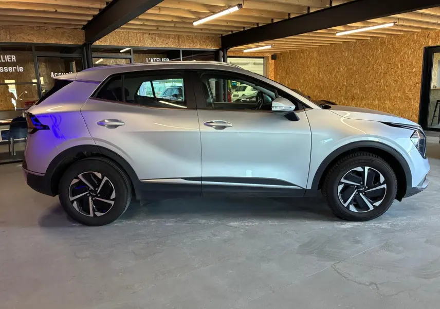 Vue de profil côté gauche d'un KIA Sportage 2024 gris hybride avec jantes noires et détails modernes.