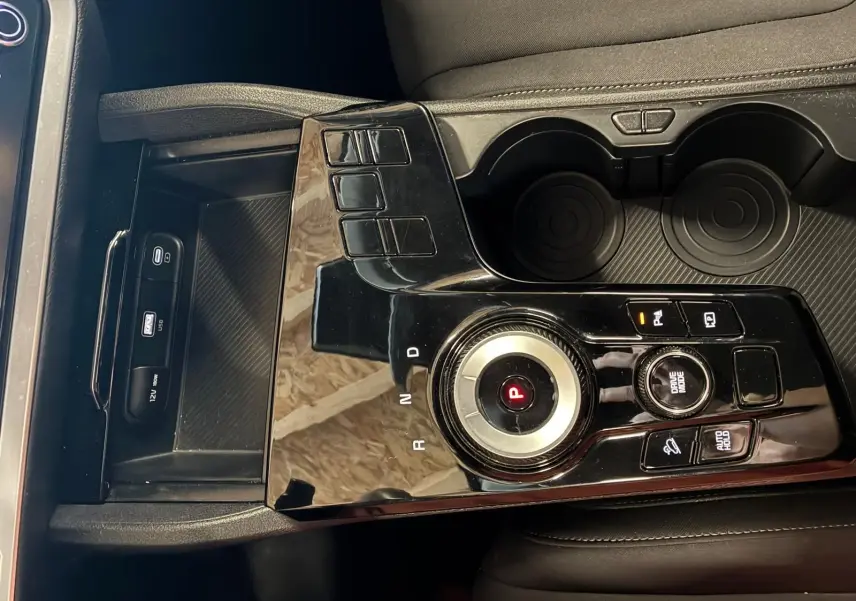Vue rapprochée de la console centrale noire brillante du Kia Sportage 2024 hybride avec molette de sélection de vitesse et porte-gobelets.