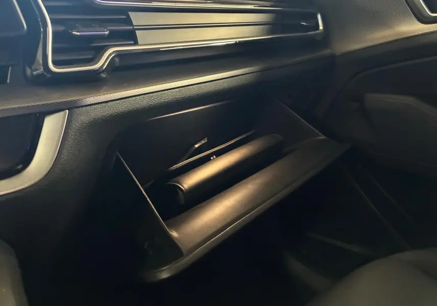 Gros plan sur la boîte à gants ouverte du Kia Sportage hybride gris 2024, côté passager avec tableau de bord noir.