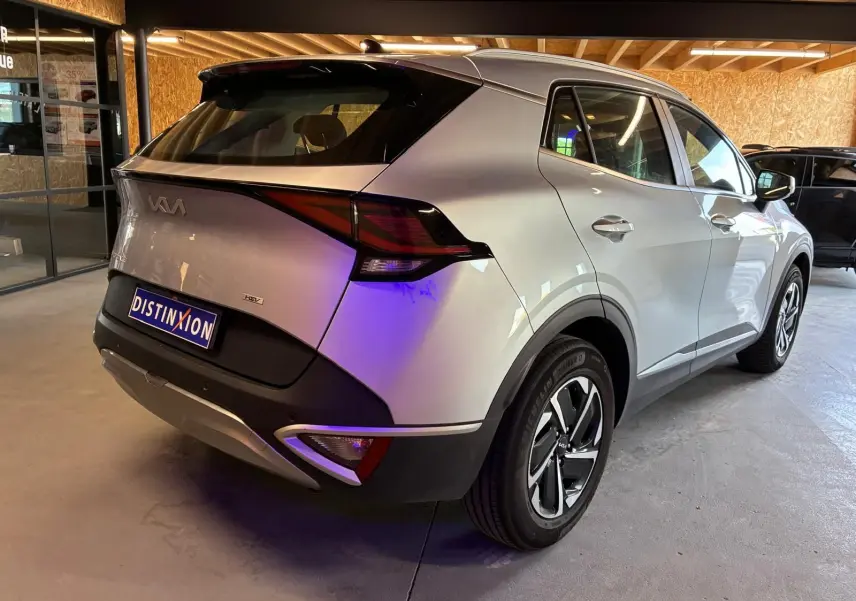 Vue 3/4 arrière droite d'un Kia Sportage gris hybride 2024 avec feux arrière distinctifs et jantes modernes.