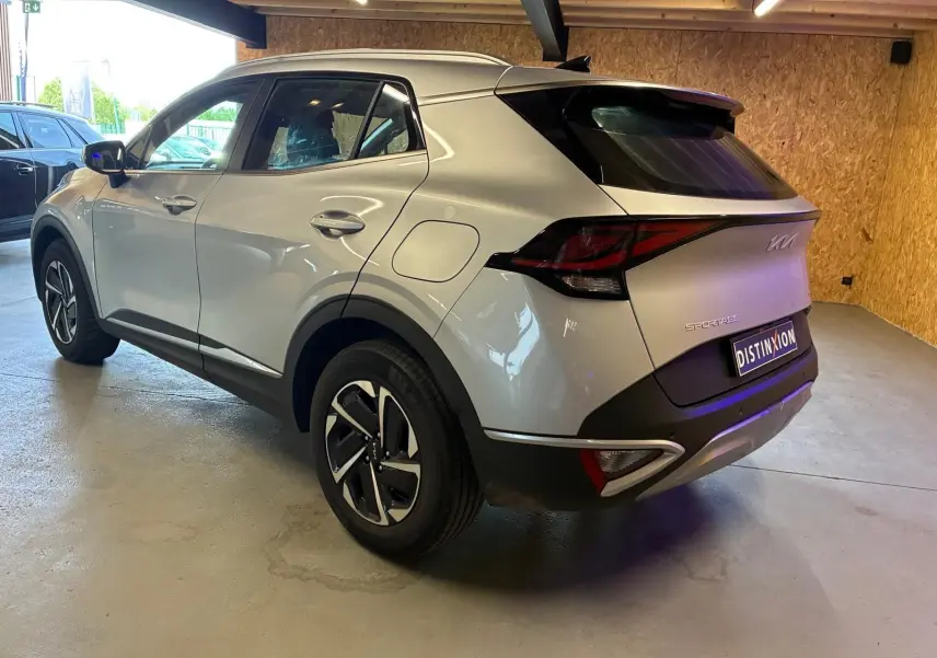 Vue 3/4 arrière droite du KIA Sportage gris 2024 hybride, avec feux arrière distinctifs et jantes bicolores.