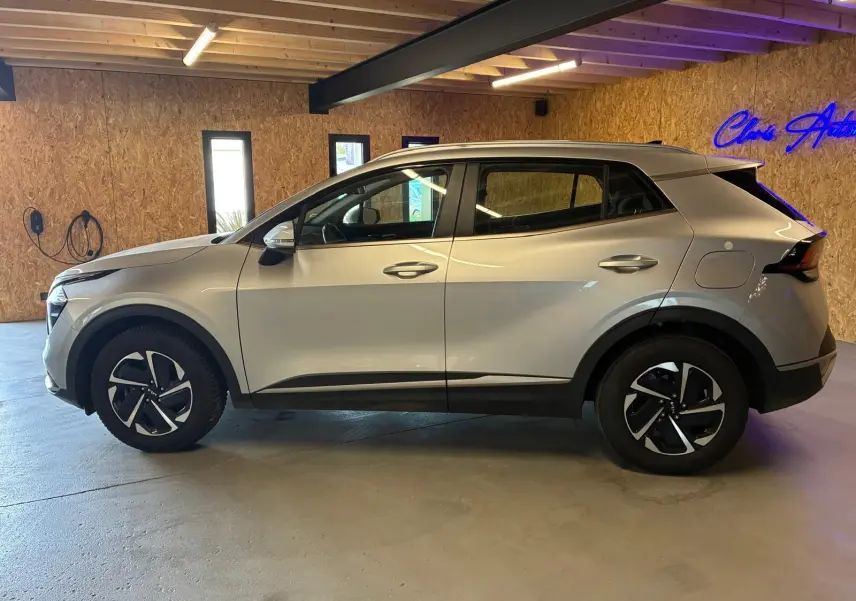 Vue de profil côté gauche du KIA Sportage 2024 gris hybride, avec jantes noires et détails noirs contrastants.
