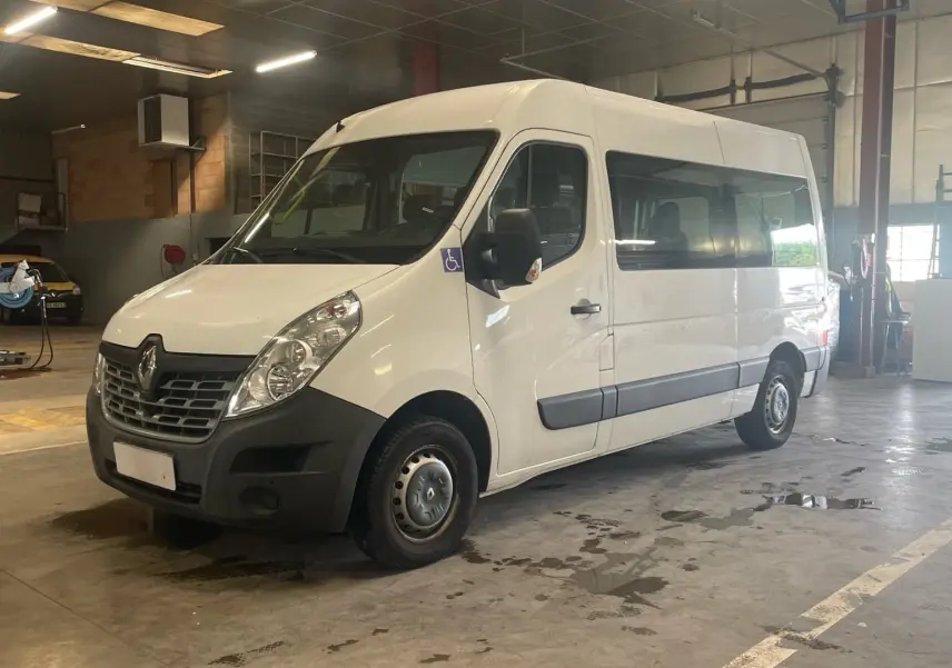 Renault Master blanc vu en 3/4 avant droit dans un garage, avec logo handicap sur la porte côté conducteur.