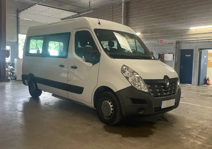 Renault Master blanc en 3/4 avant droit dans un garage, avec grandes fenêtres latérales et marchepied visible.