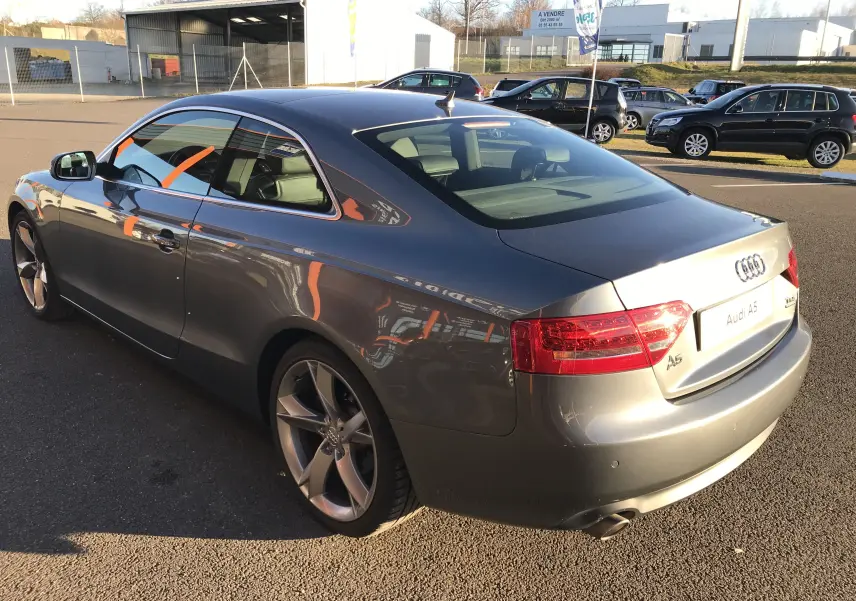 Audi A5 Coupé gris dauphin vu en 3/4 arrière droit, soulignant ses jantes alliage et lignes élégantes.