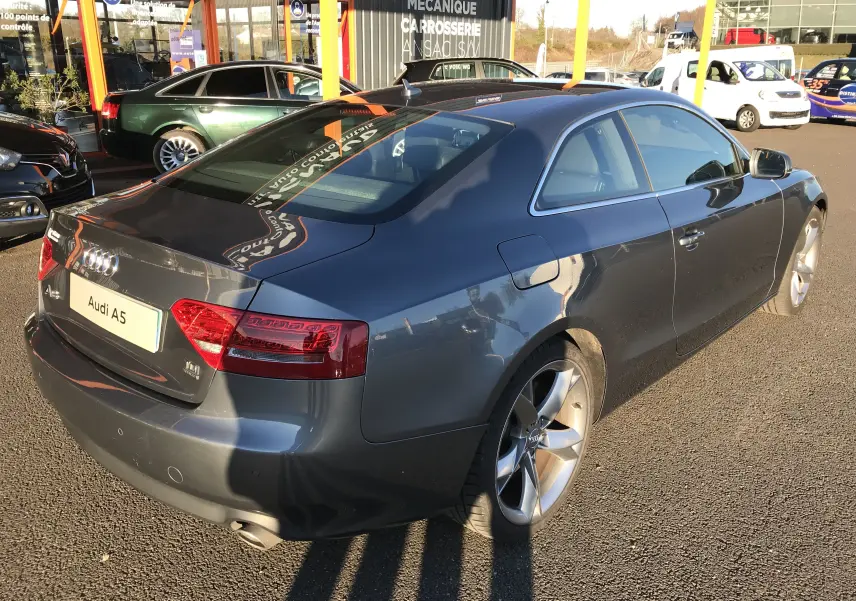 Audi A5 Coupé gris dauphin vu en 3/4 arrière droit, avec jantes alliage et feux arrière LED visibles.