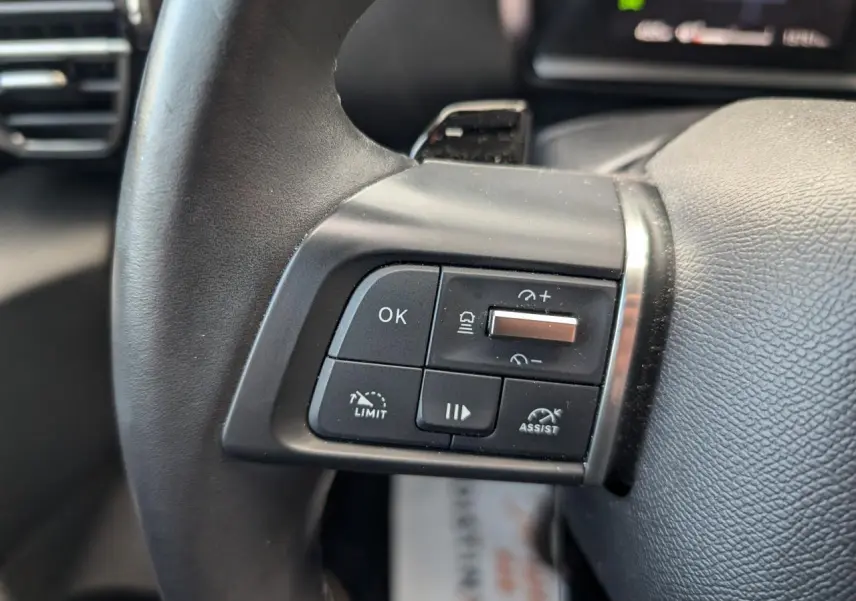 Gros plan sur les commandes de régulateur et assistant de conduite au volant cuir du Citroën C4 rouge foncé 2024.