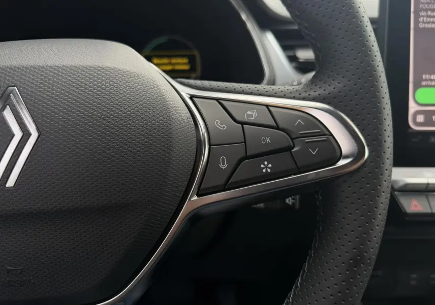 Gros plan sur la partie droite du volant perforé noir du Renault Captur gris Rafale, avec commandes multifonctions visibles.