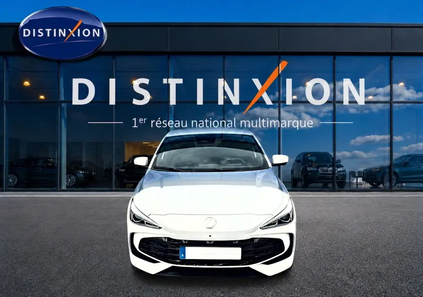 Vue avant d'une MG3 1.5 hybrid blanche stationnée devant une vitrine avec logo Distinxion.