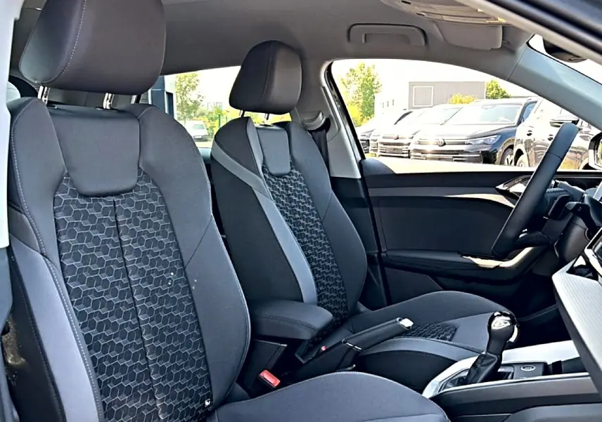 Vue intérieure avant de l’Audi A1 Sportback 30 TFSI 2026, sièges sport gris à motifs hexagonaux et accoudoir central.