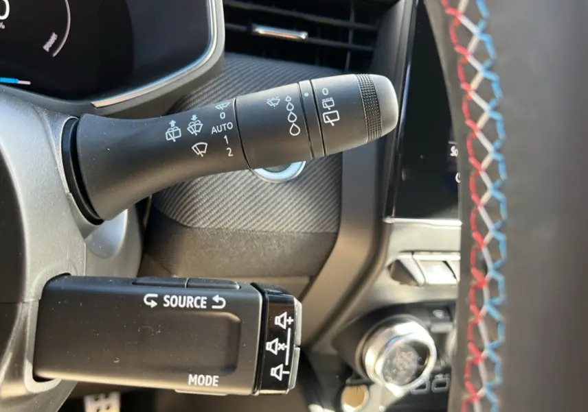 Gros plan sur le commodo gauche et volant avec surpiqûres tricolores de la Renault Clio V E-Tech 145 Esprit Alpine.