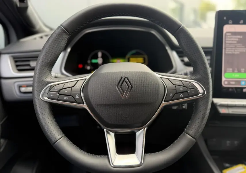 Gros plan sur le volant en cuir perforé du Renault Captur 2026, avec commandes intégrées et tableau de bord numérique flou.