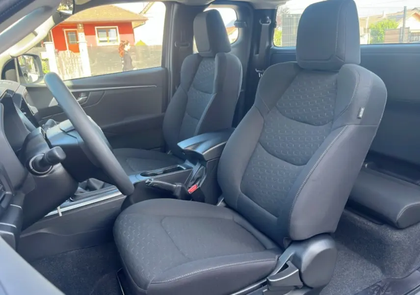 Vue intérieure côté gauche du pick-up Isuzu D-MAX 2026, sièges tissu gris foncé avec accoudoir central avant.