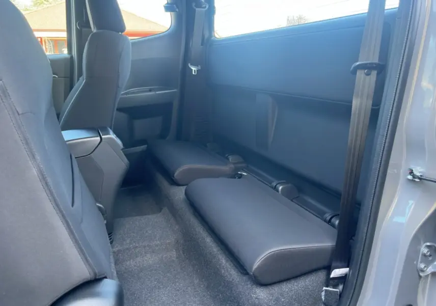 Vue intérieure côté arrière droit du pick-up Isuzu D-MAX 2026 gris Kinabalu avec strapontins rabattus et sièges tissu noirs.