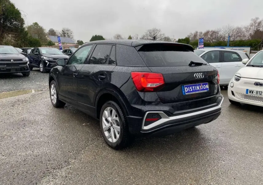 Audi Q2 noire vue 3/4 arrière droit sous la pluie, avec jantes alliage et feux arrière rouges visibles.