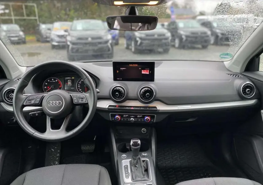 Vue intérieure avant de l'Audi Q2 2023 noire, tableau de bord avec écran central, volant multifonction et climatisation automatique.