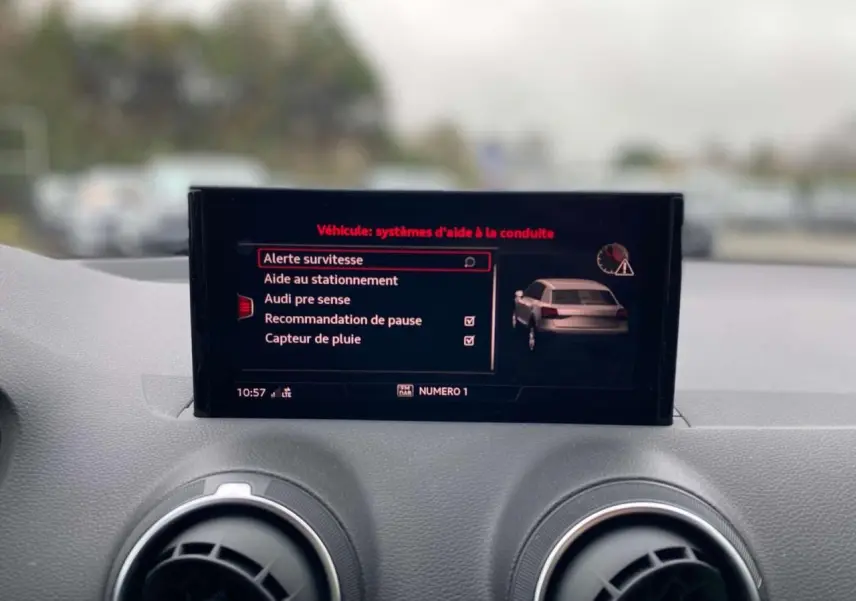Écran central de l'Audi Q2 2023 affichant les aides à la conduite, avec tableau de bord gris en arrière-plan.