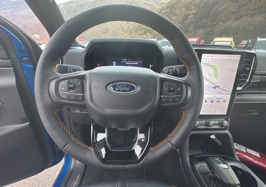 Vue intérieure centrée sur le volant cuir noir avec surpiqûres orange du Ford Ranger Wildtrak 2025 bleu lightning.