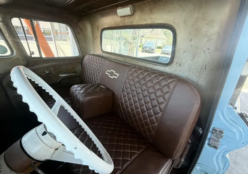 Vue intérieure côté conducteur du Chevrolet C10 Apache 1963 bleu, montrant le volant blanc et la banquette marron matelassée avec logo Chevrolet.