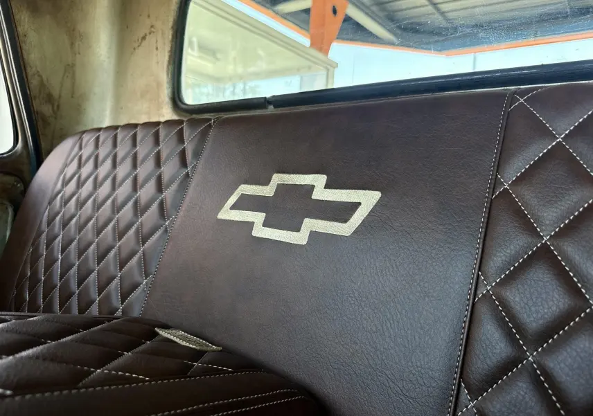 Gros plan sur la banquette arrière en cuir marron matelassé avec logo Chevrolet brodé, intérieur d’un C10 1963.