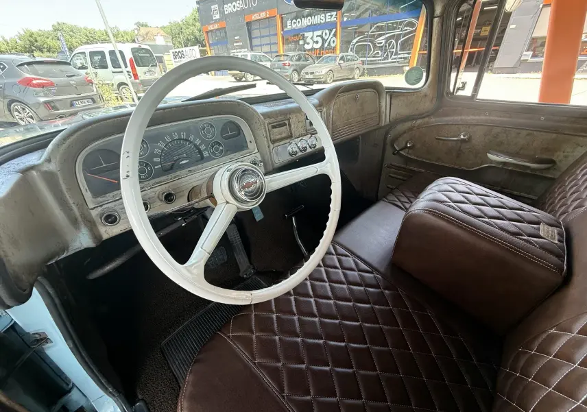 Intérieur vintage du Chevrolet C10 Apache 1963, vue côté conducteur avec volant blanc et sièges marron matelassés.
