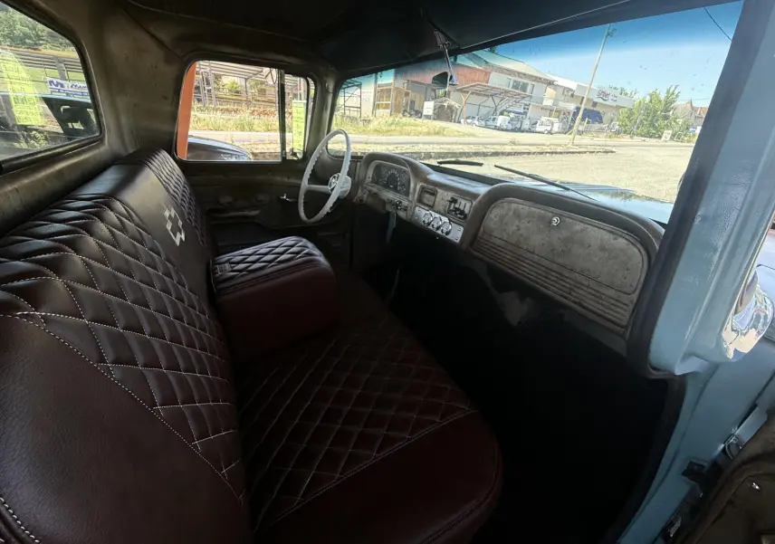 Intérieur vu côté conducteur d’un Chevrolet C10 Apache 1963 bleu, avec banquette marron matelassée et volant blanc.