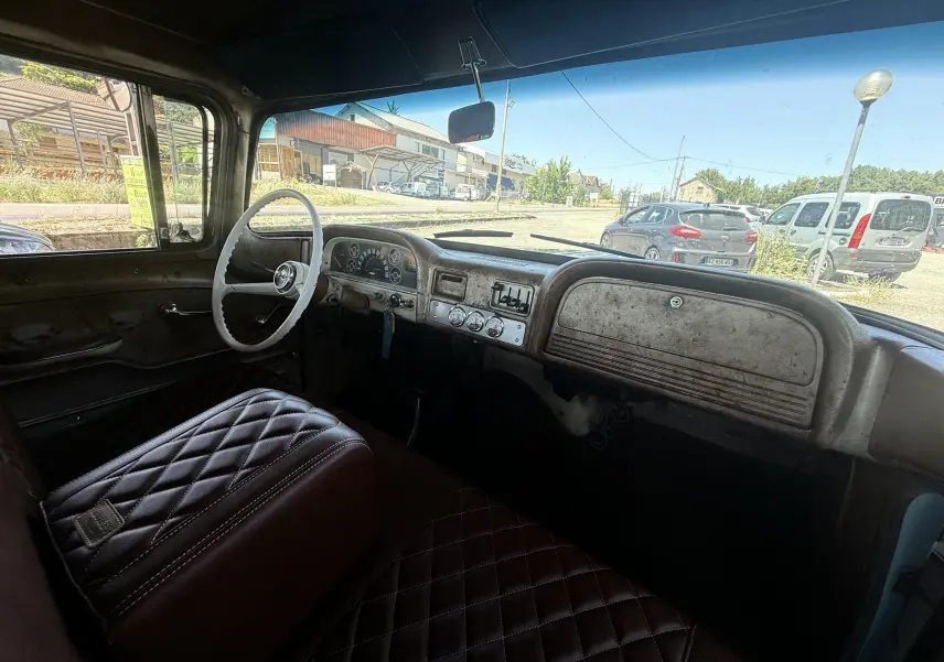 Vue intérieure côté conducteur du tableau de bord et volant blanc d’un Chevrolet C10 Apache 1963 avec sellerie marron matelassée.