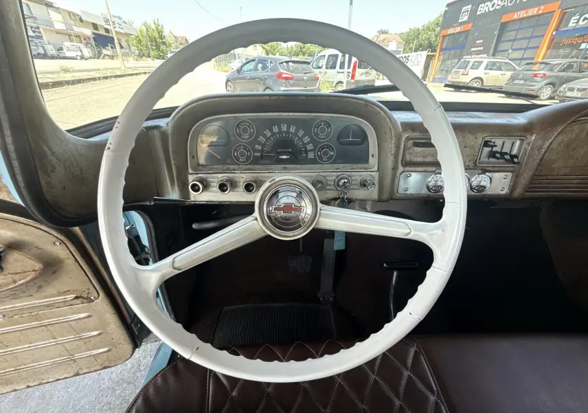 Vue intérieure centrée sur le volant blanc et le tableau de bord patiné du Chevrolet C10 Apache 1963 bleu.