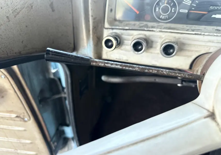 Gros plan sur la colonne de direction et le tableau de bord beige patiné d’un Chevrolet C10 Apache 1963, porte ouverte côté gauche.