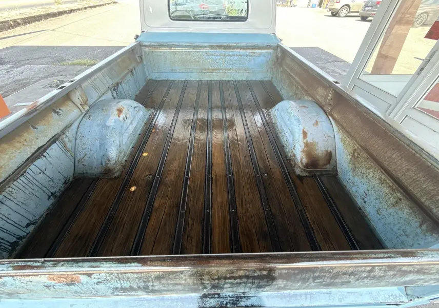 Vue plongeante sur la benne en bois patiné du pick-up Chevrolet C10 Apache 1963 bleu, montrant l'usure et la rouille.