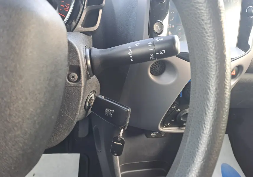 Vue rapprochée du volant noir d'une Peugeot 108 2020 avec clé insérée et commandes d'essuie-glace visibles.