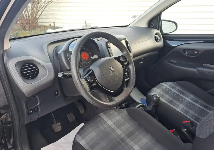 Intérieur noir de la Peugeot 108 2020, vue côté conducteur montrant volant, tableau de bord et sièges en tissu à motifs.
