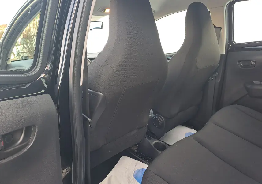 Vue intérieure arrière côté gauche d'une Peugeot 108 noire, montrant les sièges en tissu noir et la porte arrière ouverte.